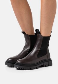 Brown leather ankle boots with elastic side panels, textured rubber sole, and pull tabs. Rounded toe and sturdy, chunky heel.