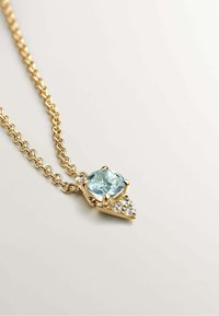 Collar de cadena de oro con un colgante ovalado de gema azul claro, adornado con piedras de acento transparentes y un diseño geométrico.