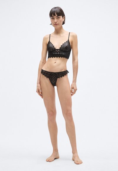 Čierny súbor čipkovanej bielizne so zubatým vzorom a geometrickým motívom. Podprsenka má kostice a nastaviteľné ramienka; zodpovedajúce bikinové nohavičky.