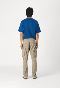 Camiseta de algodón azul de manga corta, combinada con pantalones cargo beige que cuentan con múltiples bolsillos laterales y un diseño de pierna recta.