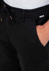 Černé cargo šortky vyrobené z bavlněné tkaniny, s elastickým pasem na šňůrku, bočními kapsami a malou značkovou nášivkou.