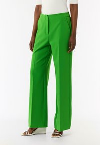 Zielone spodnie szerokie z gładką teksturą, z fałdami z przodu i dopasowanym krojem. Połączone z białymi sandałami na koturnie.