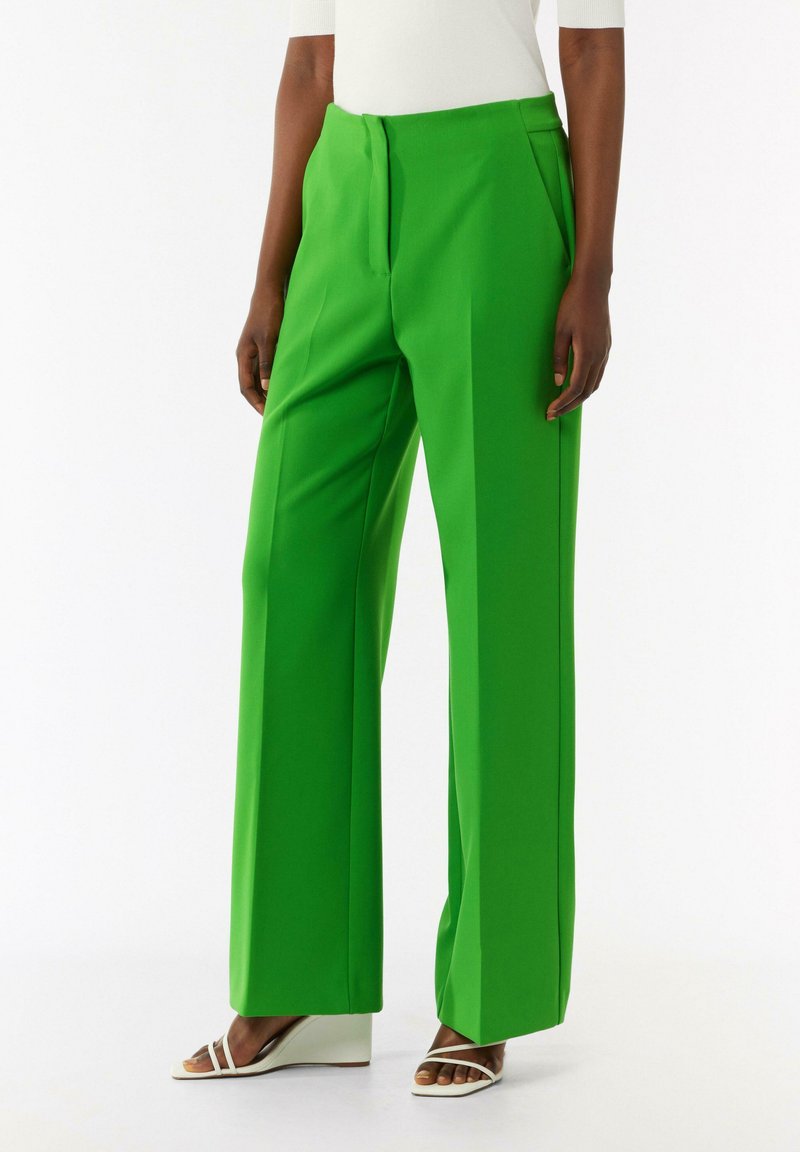 Zielone spodnie szerokie z gładką teksturą, z fałdami z przodu i dopasowanym krojem. Połączone z białymi sandałami na koturnie.