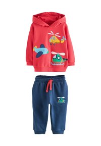 Felpa rossa con stampe di aerei e elicotteri abbinata a pantaloni blu navy con stampa di elicotteri e cordoncino rosso.