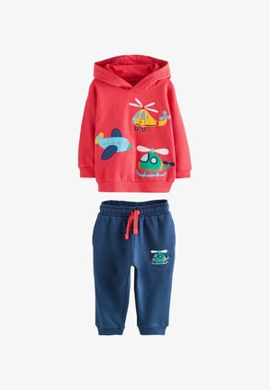 Raudonas džemperis su lėktuvų ir sraigtasparnių spauda, derinamas su tamsiai mėlynomis kelnėmis, turinčiomis sraigtasparnių spaudą ir raudoną virvutę.