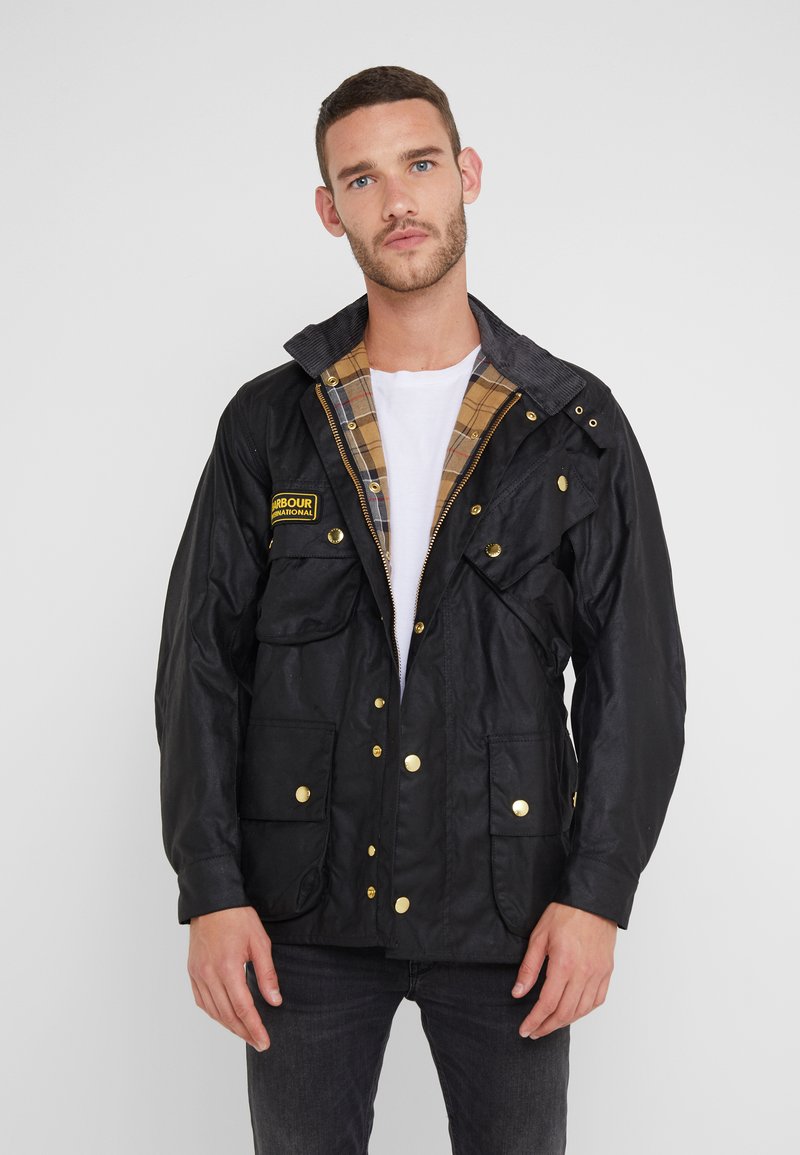 Black, waterproof jacket featuring a corduroy collar, plaid lining, multiple front pockets, and gold-tone hardware accents.