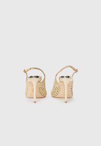 Sandali con tacco alto dorati, con design intrecciato, apertura sul retro e tacco a stiletto. Finitura liscia e dettaglio della cinturini regolabile alla caviglia.