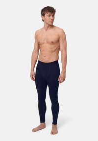 Mörkblå leggings i stretchigt material med en enkel design, med en mjuk elastisk midja. Modellen står barfota och utan tröja.