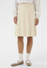 Knee-length kreemikleit, millel on ribakujundus, laienev disain ja elastne vöökoht. Kombineeritud beežide lapikute kingade ja valgete sokkidega.