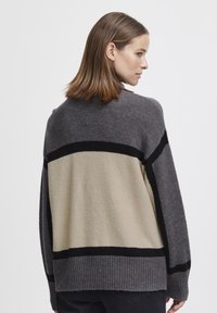 Pull en tricot gris et beige avec des rayures noires, à la coupe ample, avec des poignets côtelés et un tissu texturé, vu de dos.