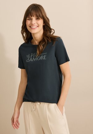 T-shirt a maniche corte di colore blu scuro realizzato in cotone; presenta la scritta "PIÙ AMORE" in un carattere chiaro sulla parte anteriore. Abbinato a pantaloni beige.