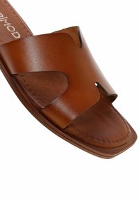 Brun lädersandaler med bred rem och utskurna mönster, slät yta och en platt, stabil sula.