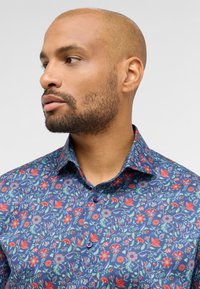 Shirt gemaakt van donkerblauw stoffen met een bloemenpatroon in rood en groen. Bevat een kraag, knoopsluiting en korte mouwen.