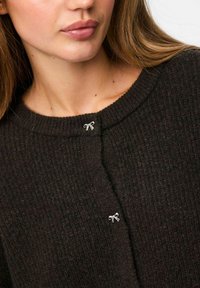 Cardigan en tricot marron avec une finition texturée, dotée d'une encolure ronde et d'un petit accent en ruban argenté au niveau du bouton supérieur.