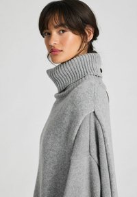 Grå turtleneck-tröja med ribbad halsringning, mjuk textur, oversized passform och design med sänkt axel. Minimalistisk stil utan mönster.