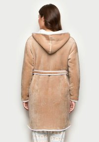 Túnica beige con capucha hecha de una suave tela de felpa, con un borde blanco, ceñida a la cintura con un cinturón a juego, mostrada desde la parte de atrás.