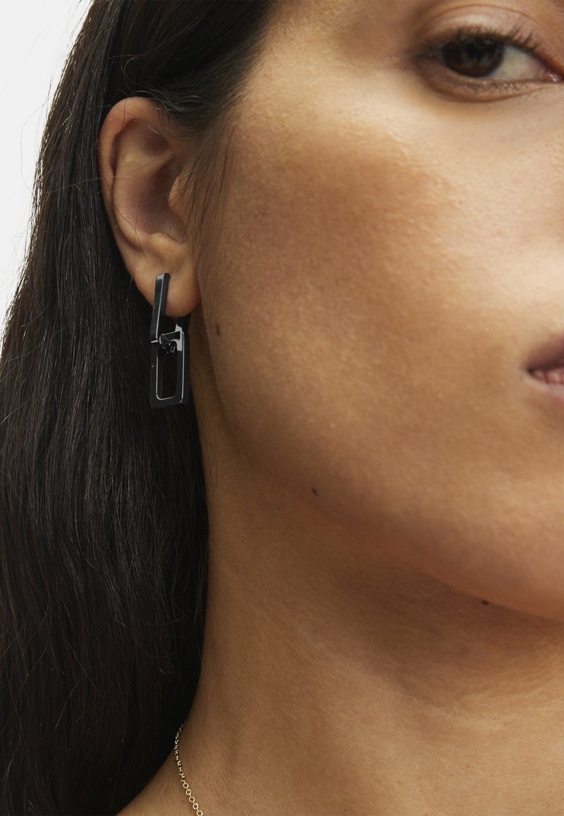 Schwarze geometrische Ohrringe mit einem geschichteten Design in rechteckiger und quadratischer Form, aus einem glatten Material gefertigt.