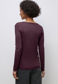 Long-sleeve shirt in deep maroon, featuring a wide neckline and a smooth texture, paired with gray textured trousers.