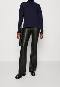 Maglione a collo alto navy con orlo a coste, abbinato a pantaloni a campana in faux pelle nera e stivali neri con tacco spesso. Borsa a tracolla nera.