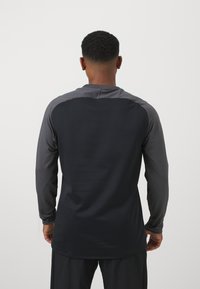 Maglietta atletica a maniche lunghe in grigio scuro e nero, con una texture liscia che presenta cuciture a contrasto sulle spalle e un colletto rotondo.