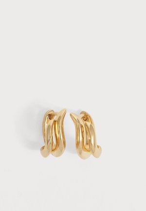 Paire de boucles d'oreilles créoles torsadées dorées brillantes avec un design lisse et incurvé sur un fond blanc uni.