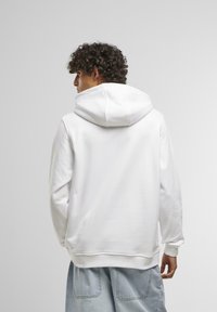 Sweatshirt à capuche blanche avec une texture douce, comportant une poche kangourou et des poignets côtelés, associé à un short en denim bleu clair.