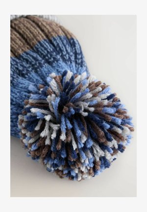 Pletená čiapka s modro-hnedo-krémovou farebnou paletou, s veľkým viacfarebným pom-pomom na vrchu a rebrovanou textúrou.