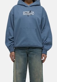 Light blue oversized hoodie with a front pocket, featuring the text "GOOD FOR NOTHING" in white and black. Ribbed cuffs and soft fabric.