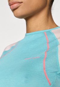 Αθλητική μπλούζα ανοιχτού γαλάζιου χρώματος με ροζ λεπτομέρειες, διαθέτει επίπεδες ραφές και στρογγυλή λαιμόκοψη, κατασκευασμένη από ελαστικό, διαπνέον υλικό.