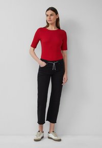 Rood geribbelde T-shirt met korte mouwen gecombineerd met zwarte cropped broeken met een trekkoord in de taille, gedragen met beige en witte sneakers.