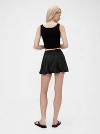 Svart ribbad crop top matchad med en högmidjad svart plisserad kjol. Minimalistisk design med mjuk textur och platta sandaler.