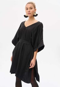 Schwarzes, knielanges Kleid mit V-Ausschnitt, übergroßen Ärmeln und tailliertem Gürtel. Glatter Stoff mit seitlichen Schlitzen für mehr Bewegungsfreiheit.