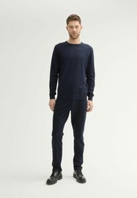 Pull en tricot bleu marine et pantalon assorti. Le pull présente un col rond et des manches longues, complété par des chaussures noires.