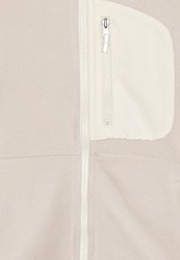 Giacca beige chiaro con zip, caratterizzata da un tessuto testurizzato, dettagli crema e una tasca con zip sul lato sinistro superiore.