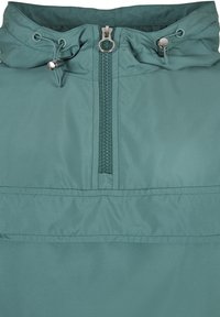 Teal windbreaker s patentnim zatvaračem sprijeda, podesivim kapuljačom s vezicom i glatkim, laganim materijalom. Ima minimalistički dizajn i suptilno šivanje.