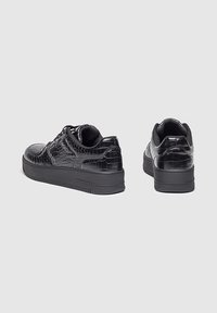 Zapatillas negras con una textura grabada de cocodrilo, punta redonda, suela gruesa de plataforma y diseño con cordones. La vista trasera muestra un detalle minimalista.