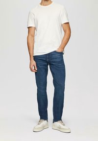 White short-sleeve t-shirt, blue slim-fit jeans, and beige low-top sneakers. Casual outfit with a simple design and classic colors.