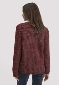 Burgunderfarbener Strickpullover mit gerippter Textur, langer Ärmel und lockerer Passform, die eine subtile Variation in der Farbgebung des Garns zeigt.