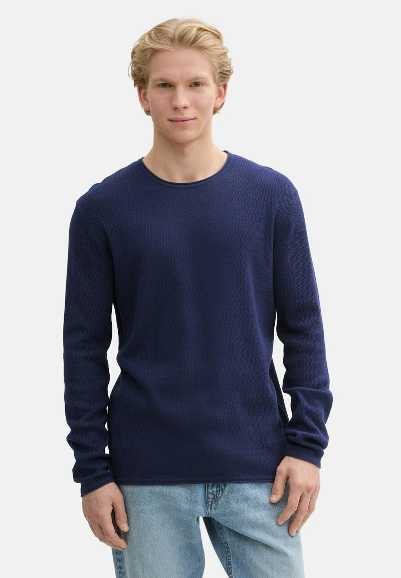 Marineblauwe lange mouwen gebreid t-shirt met een textuurpatroon, ronde halslijn en een iets lose pasvorm, gecombineerd met lichtblauwe denim jeans.