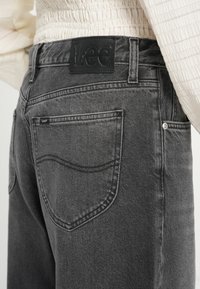 Jeans in denim grigio con una texture liscia, dotati di un'etichetta in pelle nera con "Lee" sulla vita e due tasche posteriori con cuciture curve.