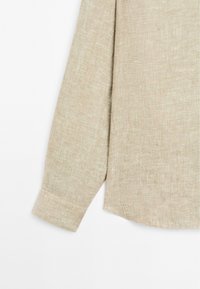 Beige linen long-sleeve shirt with a textured finish, featuring a single cuff and straight hem. Subtle woven pattern.