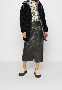 Chaqueta de plumas negra con un patrón de Mickey Mouse, un jersey de cuello alto con flores, una falda midi de cuero y unos mocasines gruesos beige con suelas negras.