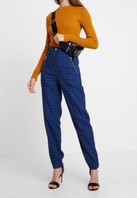 Ribbad senapsgul tröja i kombination med blå rutiga byxor med dragkedjefickor och en svart axelväska. Svarta remsandaler fulländar looken.