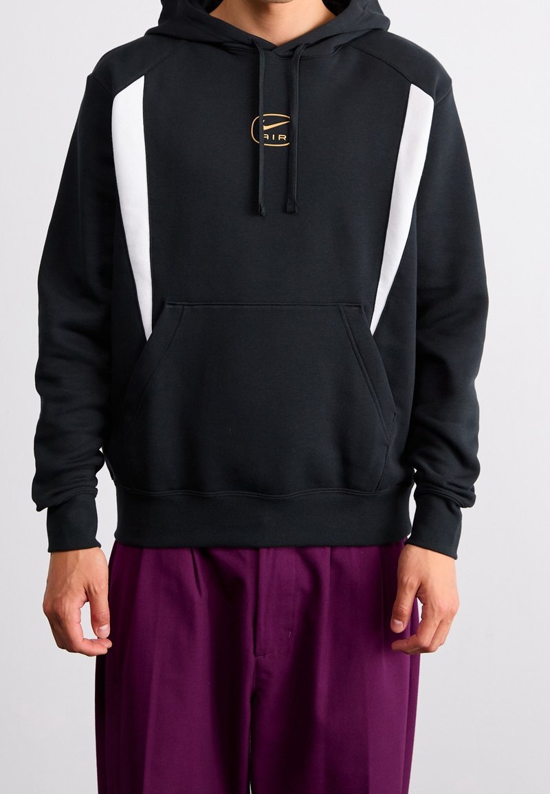 Black hoodie with white panel accents and a gold logo on the chest. Features a front pocket and ribbed cuffs. Smooth fabric texture.