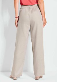 Lichtbeige wijde broek met een elastische tailleband, een gladde textuur en geen zichtbare patronen, gecombineerd met lichte schoenen.