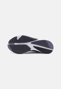 Semelle de chaussure de sport noire et blanche avec des rainures diagonales pour la traction, montrée sur un fond gris clair uni.