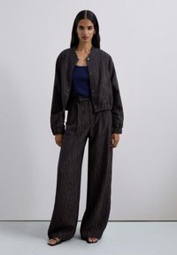 Conjunto de dos piezas que incluye una chaqueta oscura con un patrón y un cuello redondo, y pantalones de pierna ancha a juego, complementados con una camiseta sin mangas en color azul marino.