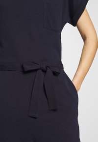 Marineblaue Latzhose mit einer Brusttasche, kurzen Ärmeln, einem taillierten Bund und seitlichen Taschen. Hergestellt aus strukturiertem Material mit lässiger Passform.