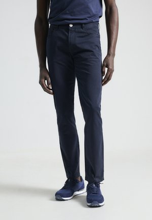 Chinos azul marino de algodón, corte slim, con cremallera, cierre de botón y bolsillos traseros. Combinados con zapatillas deportivas azules.