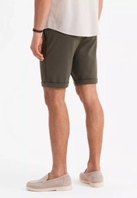 Olivgröna shorts som är gjorda av mjukt material, med upprullade fållar och sidofickor, parat med ljusbeige slip-on skor.